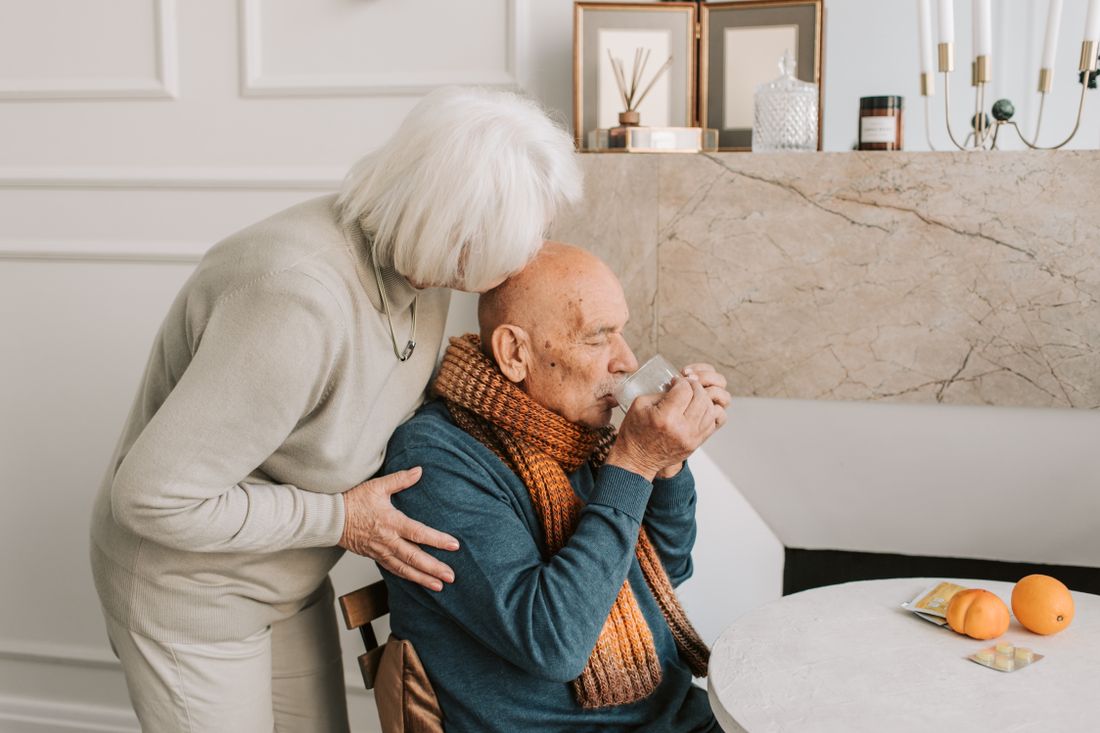 An elderly man being helped to drink a glass of water at home