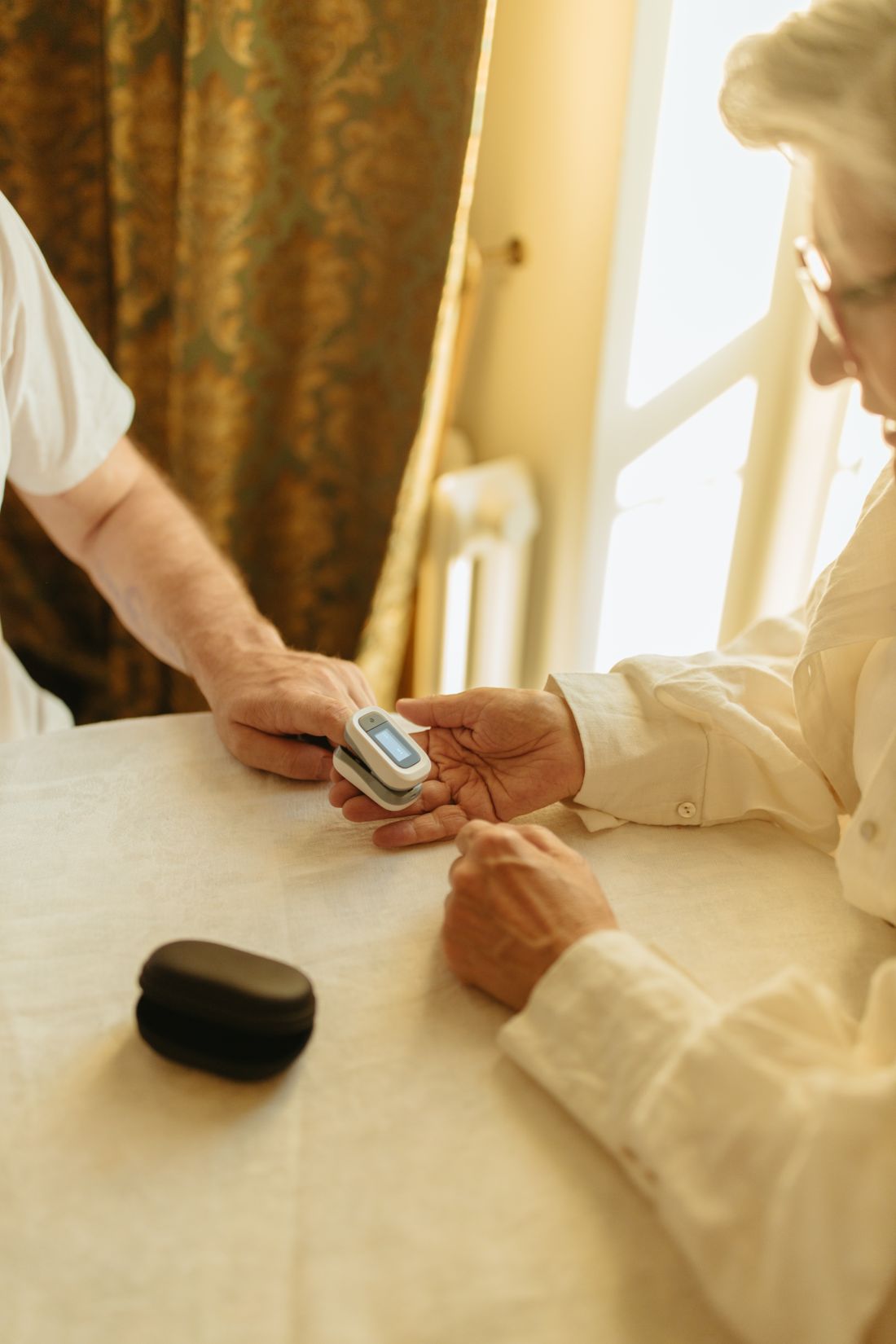 A pulse oximeter being placed on an elderly person's finger at home