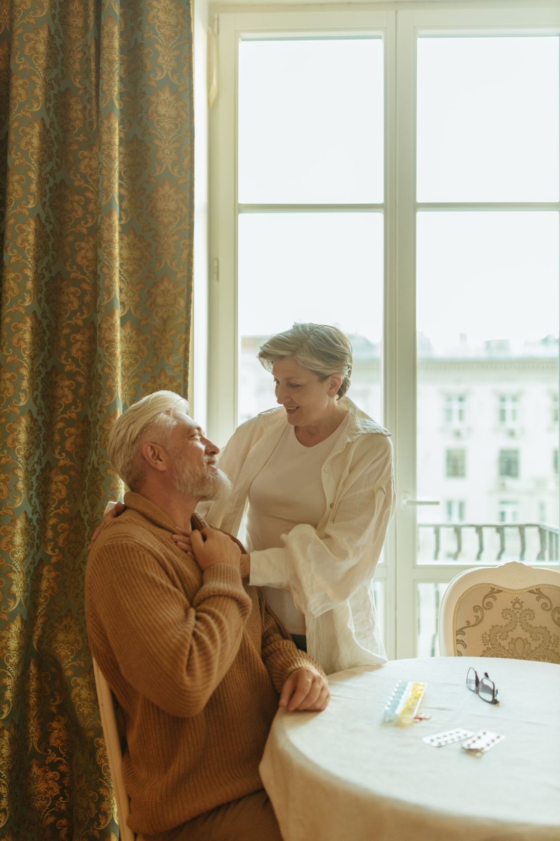 A caregiver comforting an elderly man at home by a bright window